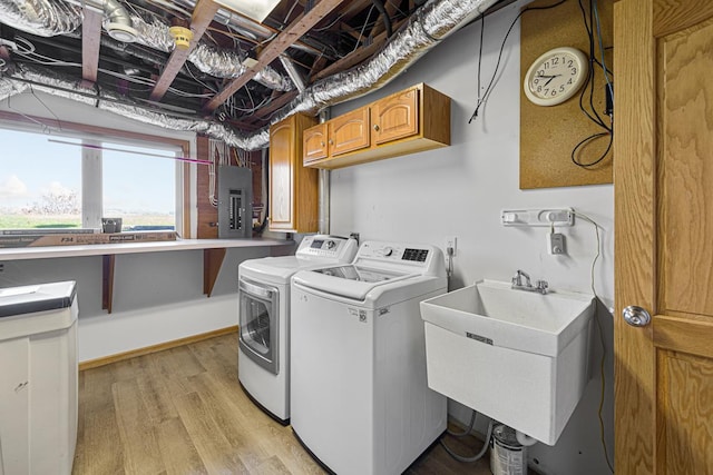 washroom with light wood-style flooring, a sink, electric panel, separate washer and dryer, and cabinet space