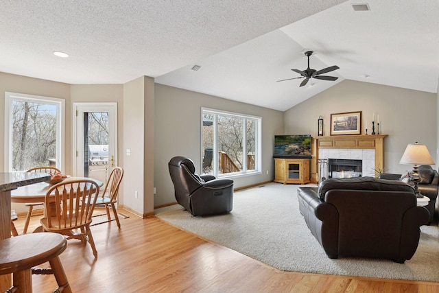 living area with a tiled fireplace, ceiling fan, light wood-type flooring, baseboards, and lofted ceiling