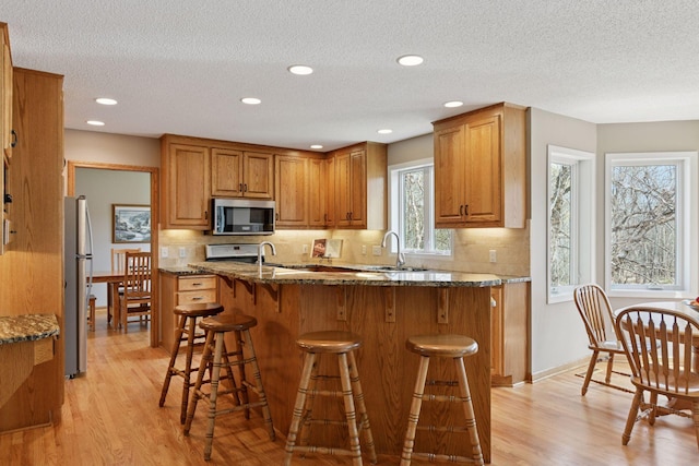 kitchen with brown cabinets, a sink, appliances with stainless steel finishes, and light wood-type flooring