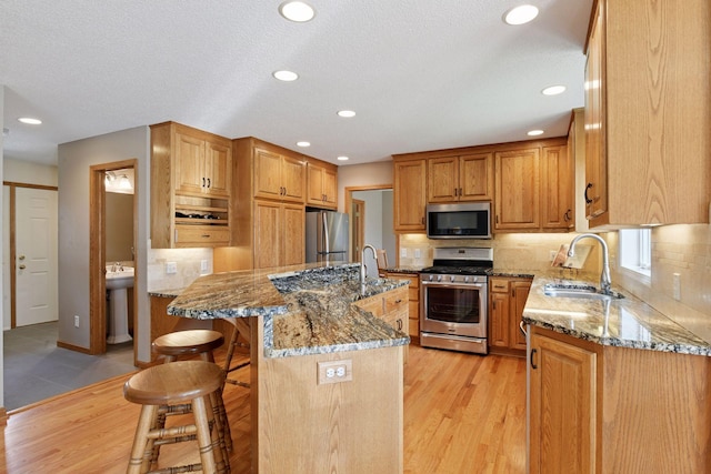 kitchen featuring light stone countertops, a sink, light wood-style flooring, and stainless steel appliances