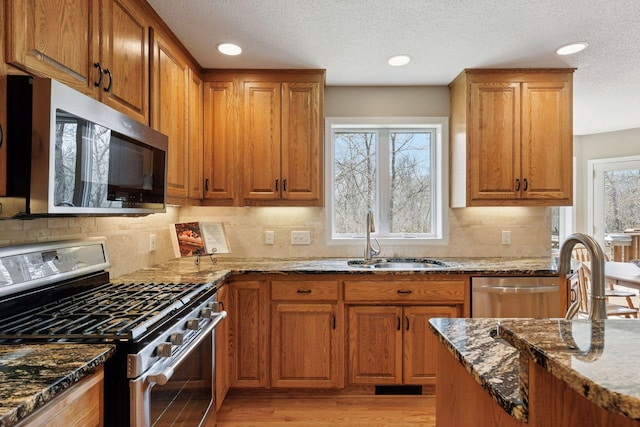 kitchen featuring dark stone counters, decorative backsplash, a sink, stainless steel appliances, and brown cabinetry