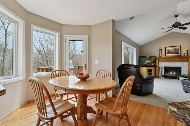 dining area featuring a tile fireplace, a healthy amount of sunlight, and light wood finished floors