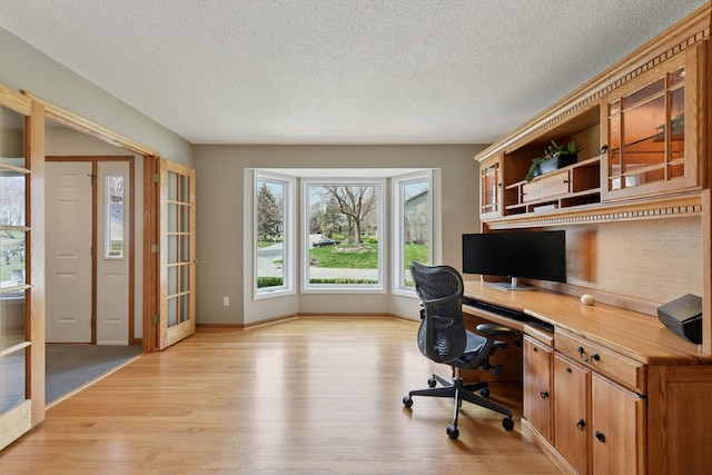 office area with a textured ceiling, light wood-style flooring, built in desk, and baseboards