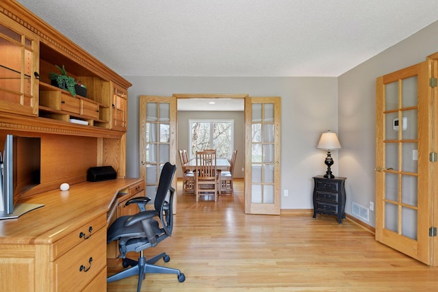 office featuring visible vents, built in study area, light wood-style flooring, baseboards, and french doors