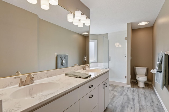 bathroom featuring wood finished floors, toilet, a shower stall, and a sink