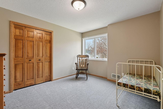 carpeted bedroom featuring a textured ceiling, visible vents, a closet, and baseboards