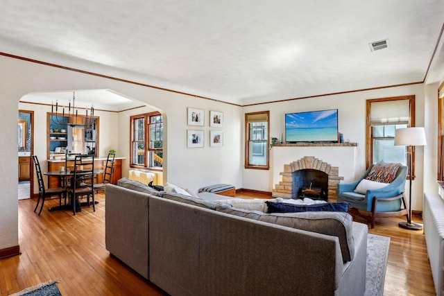 living room featuring visible vents, a fireplace, light wood-type flooring, arched walkways, and a wealth of natural light
