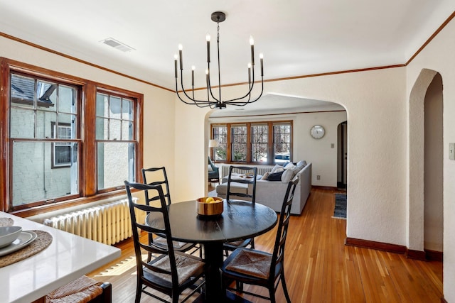 dining area with a notable chandelier, arched walkways, radiator, visible vents, and ornamental molding