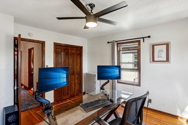 home office with wood finished floors, baseboards, radiator heating unit, a textured ceiling, and a ceiling fan