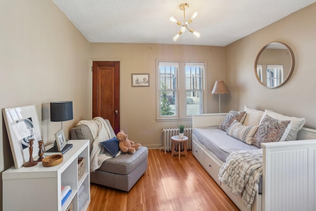 living room with an inviting chandelier, light wood finished floors, a textured ceiling, radiator, and baseboards