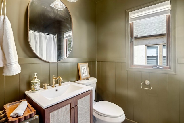 bathroom with vanity, toilet, plenty of natural light, and a wainscoted wall