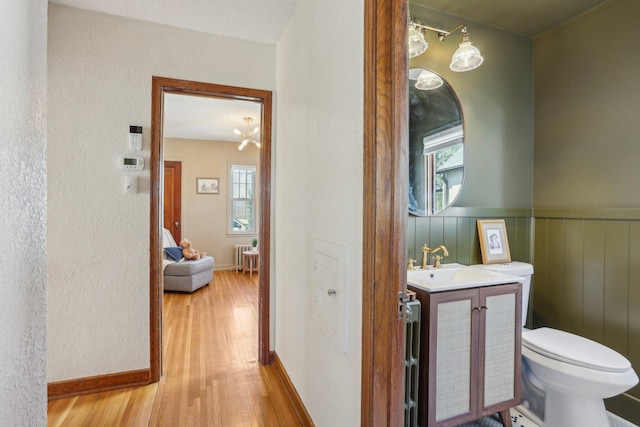 half bath with toilet, a textured wall, wood finished floors, and vanity
