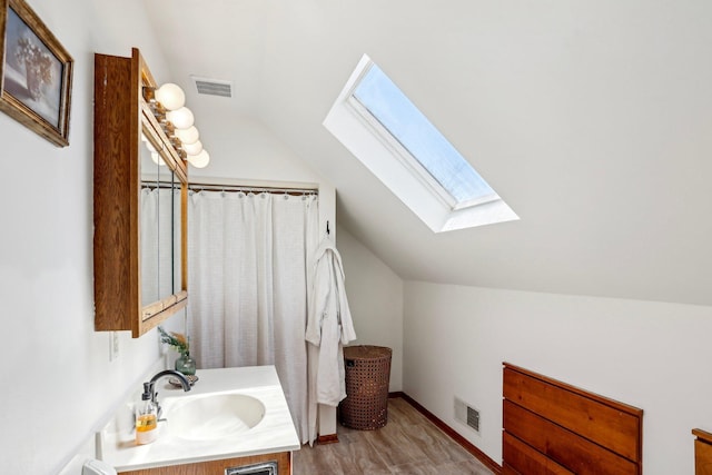 full bath with visible vents, wood finished floors, lofted ceiling with skylight, and vanity