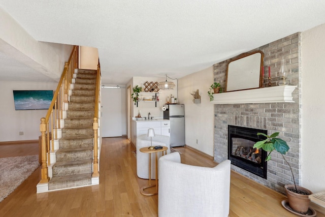 living area featuring a fireplace, stairs, and light wood-style flooring
