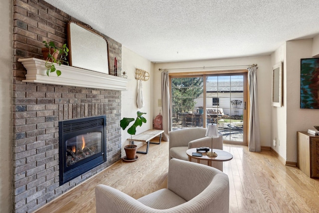 living room with a brick fireplace, a textured ceiling, baseboards, and light wood-style flooring