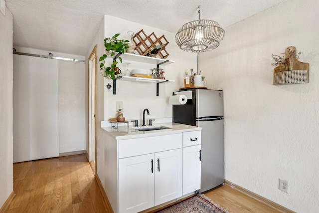 kitchen with open shelves, a sink, light wood-style floors, freestanding refrigerator, and white cabinetry