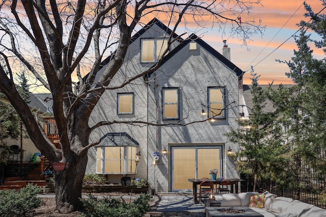 rear view of property featuring stucco siding, a chimney, and fence