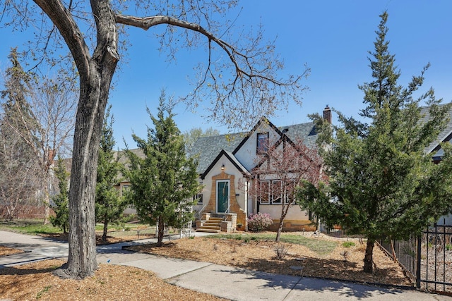 tudor house featuring stucco siding, fence, and a chimney