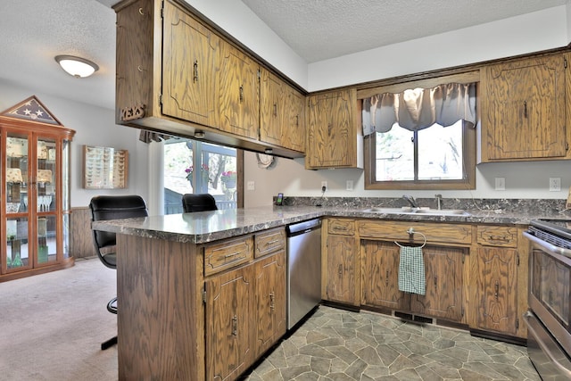 kitchen featuring a peninsula, a sink, appliances with stainless steel finishes, and a textured ceiling