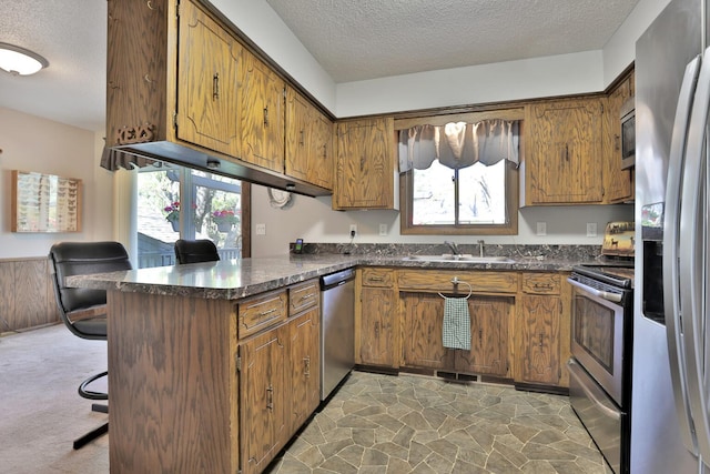kitchen featuring a peninsula, brown cabinets, a textured ceiling, dark countertops, and appliances with stainless steel finishes