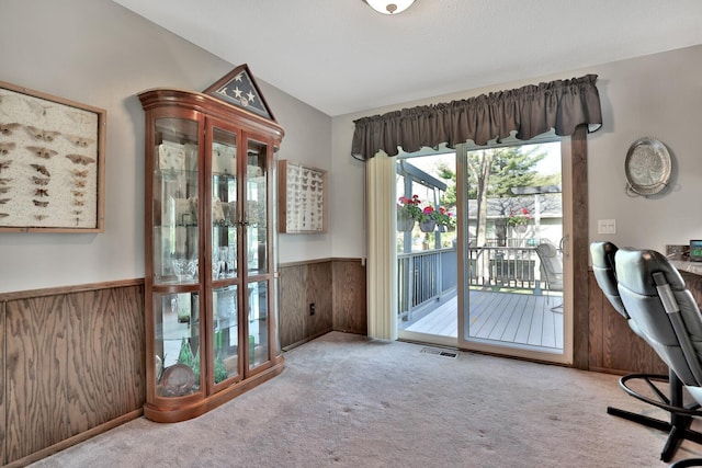 unfurnished office with wooden walls, wainscoting, visible vents, and carpet