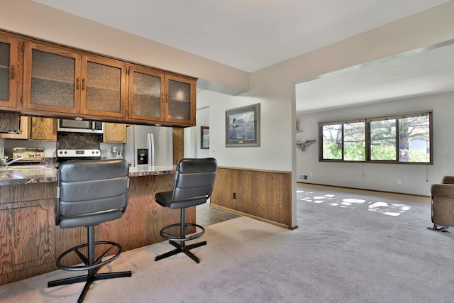 interior space featuring appliances with stainless steel finishes, light carpet, brown cabinetry, and wainscoting
