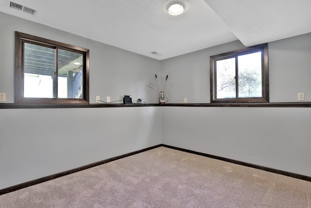 spare room with a textured ceiling, carpet floors, baseboards, and visible vents