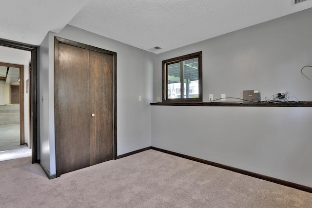 unfurnished bedroom featuring a closet, a textured ceiling, carpet, visible vents, and baseboards