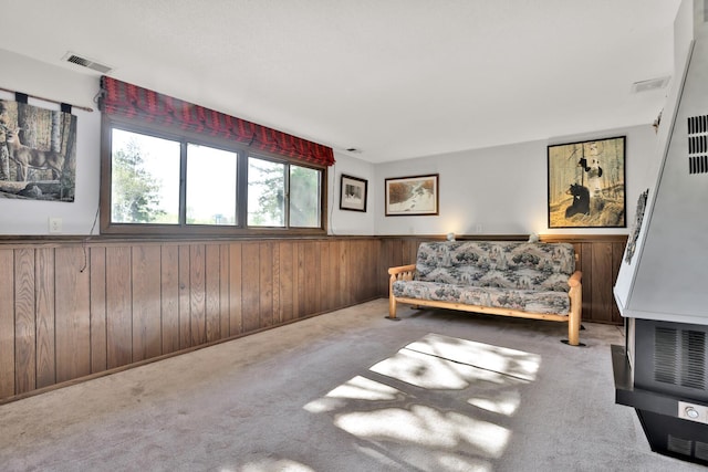 sitting room featuring carpet flooring, a heating unit, wood walls, visible vents, and wainscoting