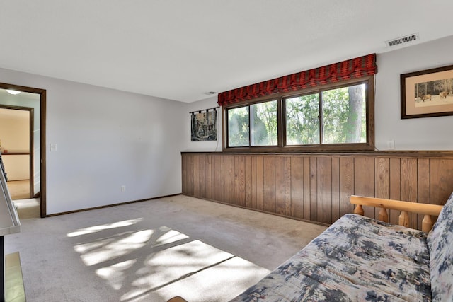 bedroom featuring wooden walls, carpet, a wainscoted wall, and visible vents