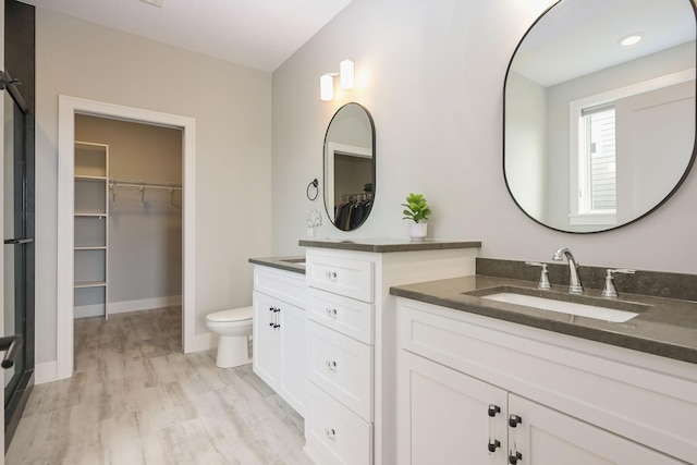bathroom featuring toilet, baseboards, two vanities, and a sink