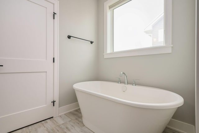 full bath featuring baseboards, wood finished floors, and a soaking tub