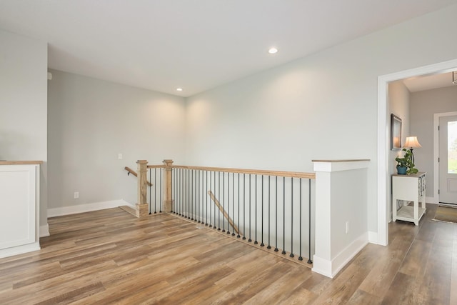 corridor featuring recessed lighting, baseboards, wood finished floors, and an upstairs landing