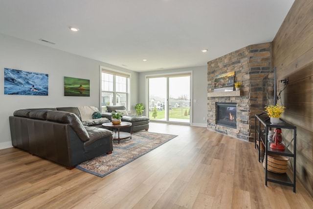 living room with baseboards, visible vents, a stone fireplace, and light wood-type flooring