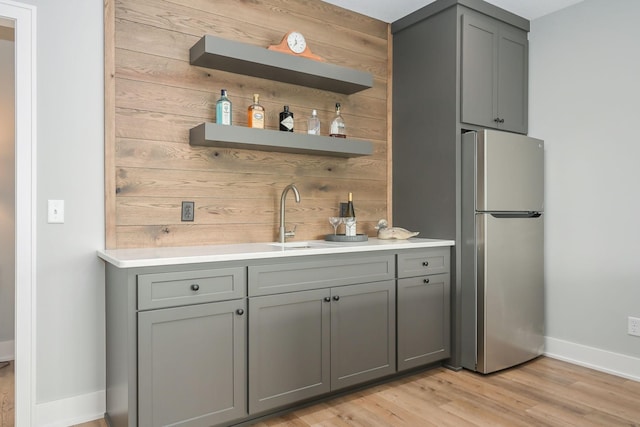 bar with wood walls, baseboards, freestanding refrigerator, indoor wet bar, and light wood-style floors