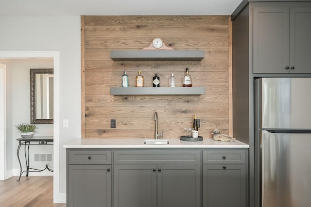 bar featuring wooden walls, a sink, freestanding refrigerator, indoor wet bar, and visible vents