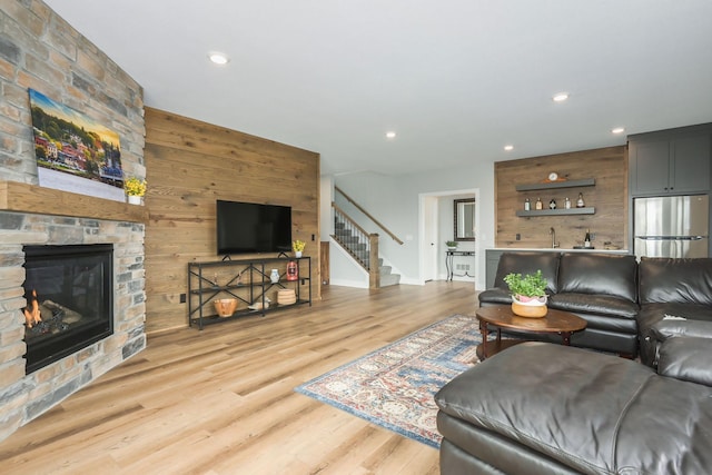 living room with wooden walls, a stone fireplace, recessed lighting, wood finished floors, and stairway