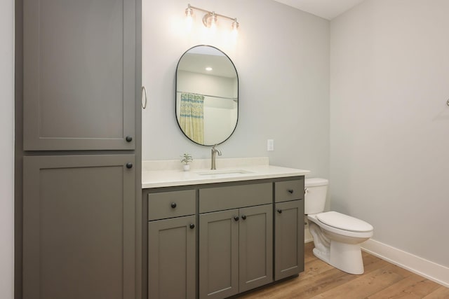 bathroom featuring baseboards, wood finished floors, toilet, and vanity