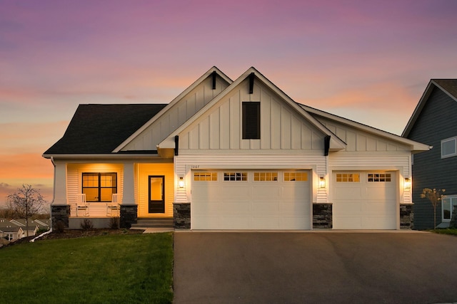 view of front of house with a front lawn, aphalt driveway, stone siding, board and batten siding, and an attached garage