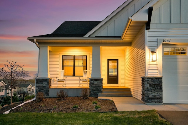 doorway to property with board and batten siding, stone siding, a shingled roof, and a porch