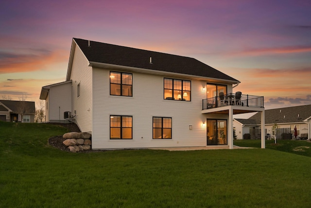 back of house at dusk featuring a yard and a balcony