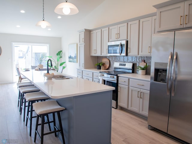 kitchen with a kitchen island with sink, backsplash, a kitchen bar, appliances with stainless steel finishes, and a sink