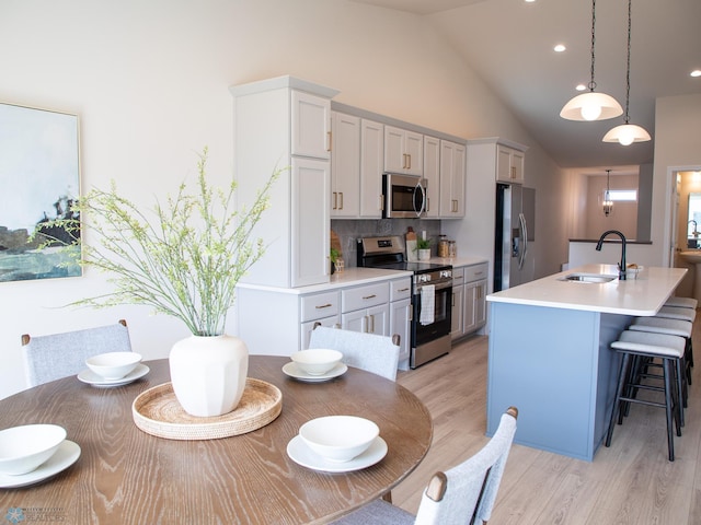 kitchen featuring a sink, light wood finished floors, light countertops, stainless steel appliances, and a center island with sink