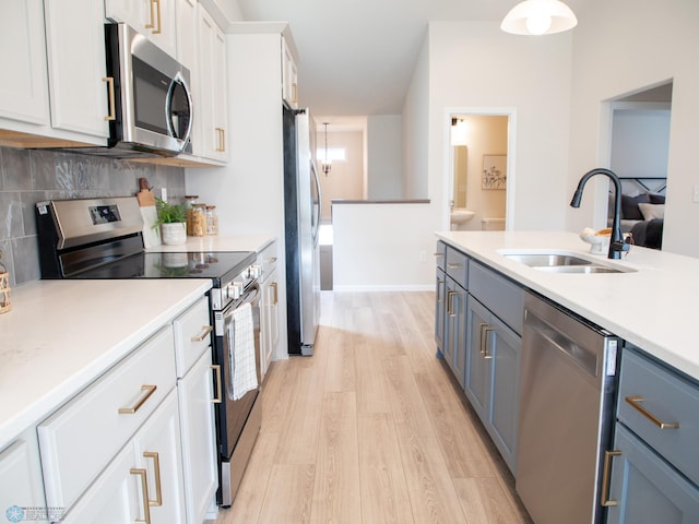 kitchen with decorative backsplash, appliances with stainless steel finishes, a sink, light countertops, and light wood finished floors