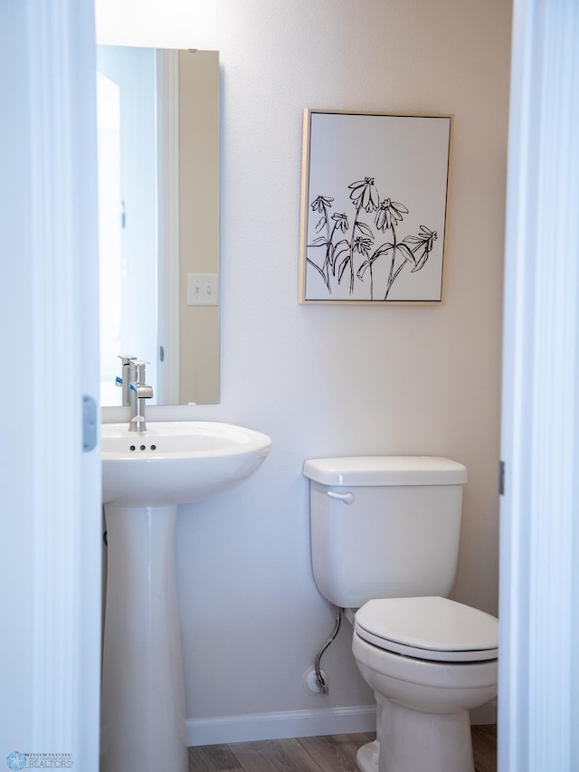 half bath with toilet, baseboards, and wood finished floors