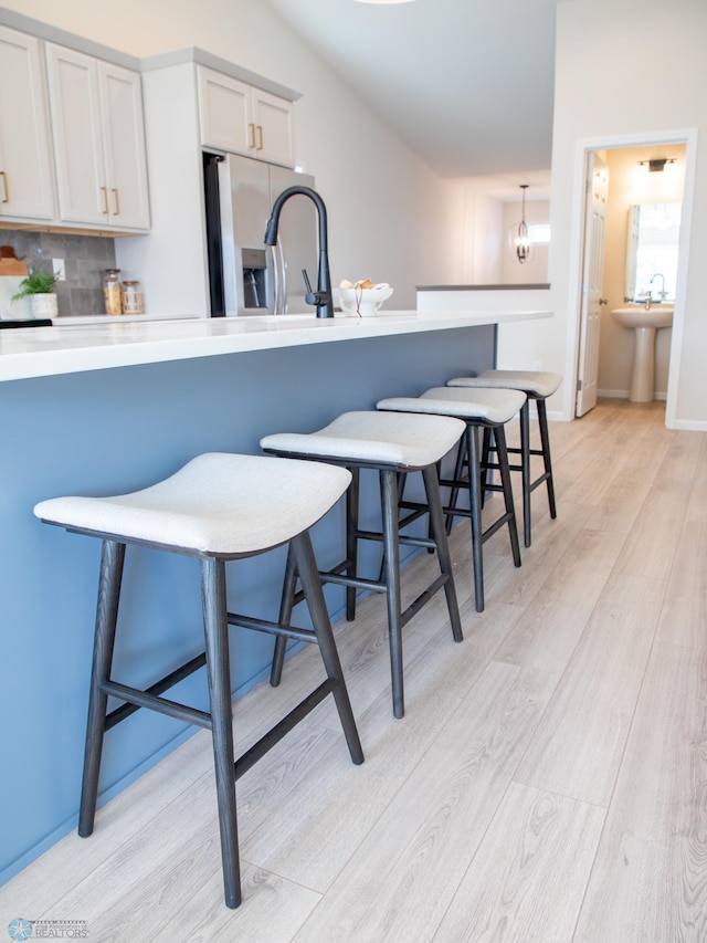 kitchen featuring decorative backsplash, a kitchen bar, stainless steel fridge, light countertops, and light wood-style flooring