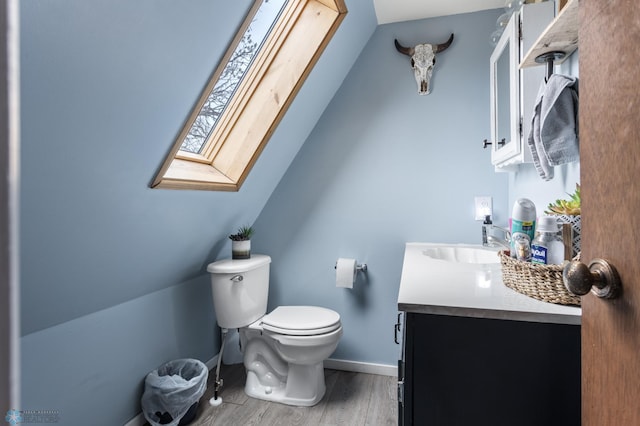 bathroom with toilet, baseboards, a skylight, wood finished floors, and vanity