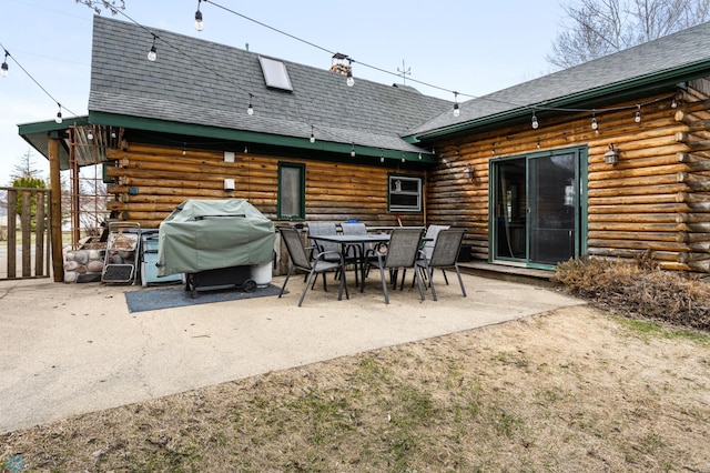 back of property with a chimney, roof with shingles, log exterior, and a patio