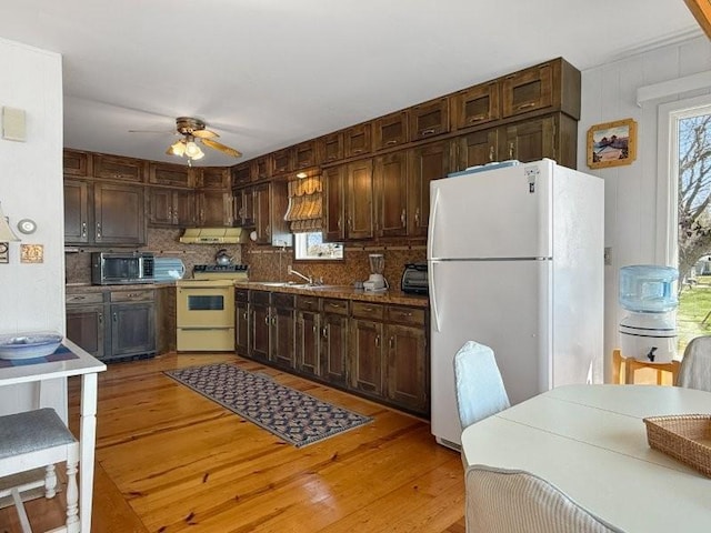 kitchen with ceiling fan, ventilation hood, backsplash, white appliances, and plenty of natural light