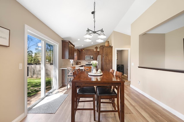 dining space featuring baseboards, light wood-style flooring, washer / clothes dryer, and lofted ceiling
